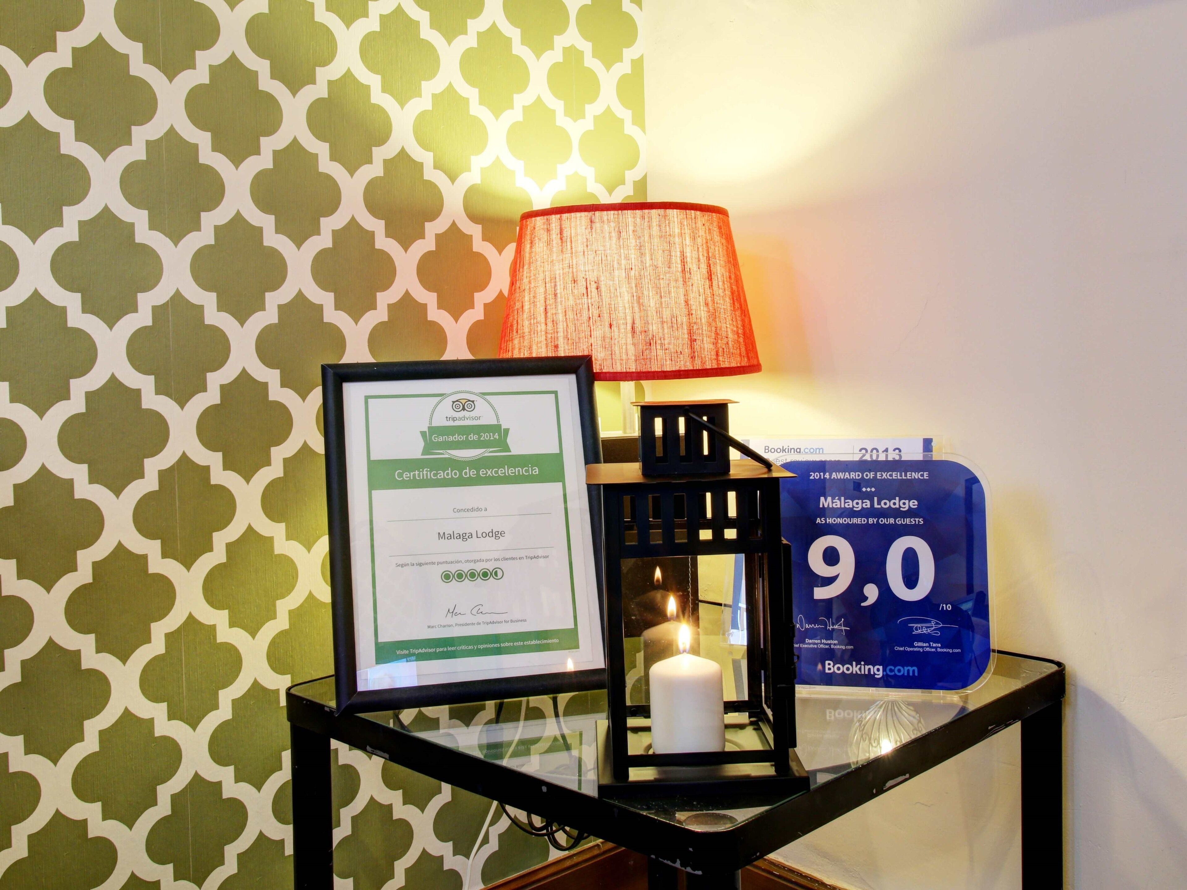 Un certificado enmarcado de premio de TripAdvisor, una vela encendida y un letrero azul con una calificación de 9.0 para Malaga Lodge.
