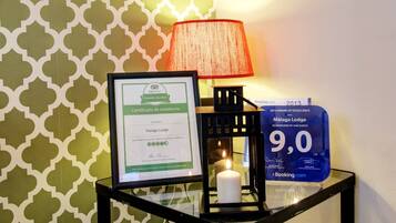 Un certificado enmarcado de premio de TripAdvisor, una vela encendida y un letrero azul con una calificación de 9.0 para Malaga Lodge.