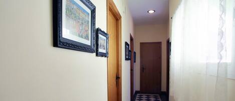 A hallway with a checkered floor, framed pictures on the walls, and a door at the end.