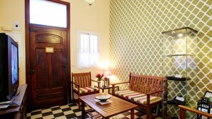Una habitación con suelo de cuadros, muebles de madera, un televisor, una puerta y papel tapiz estampado.