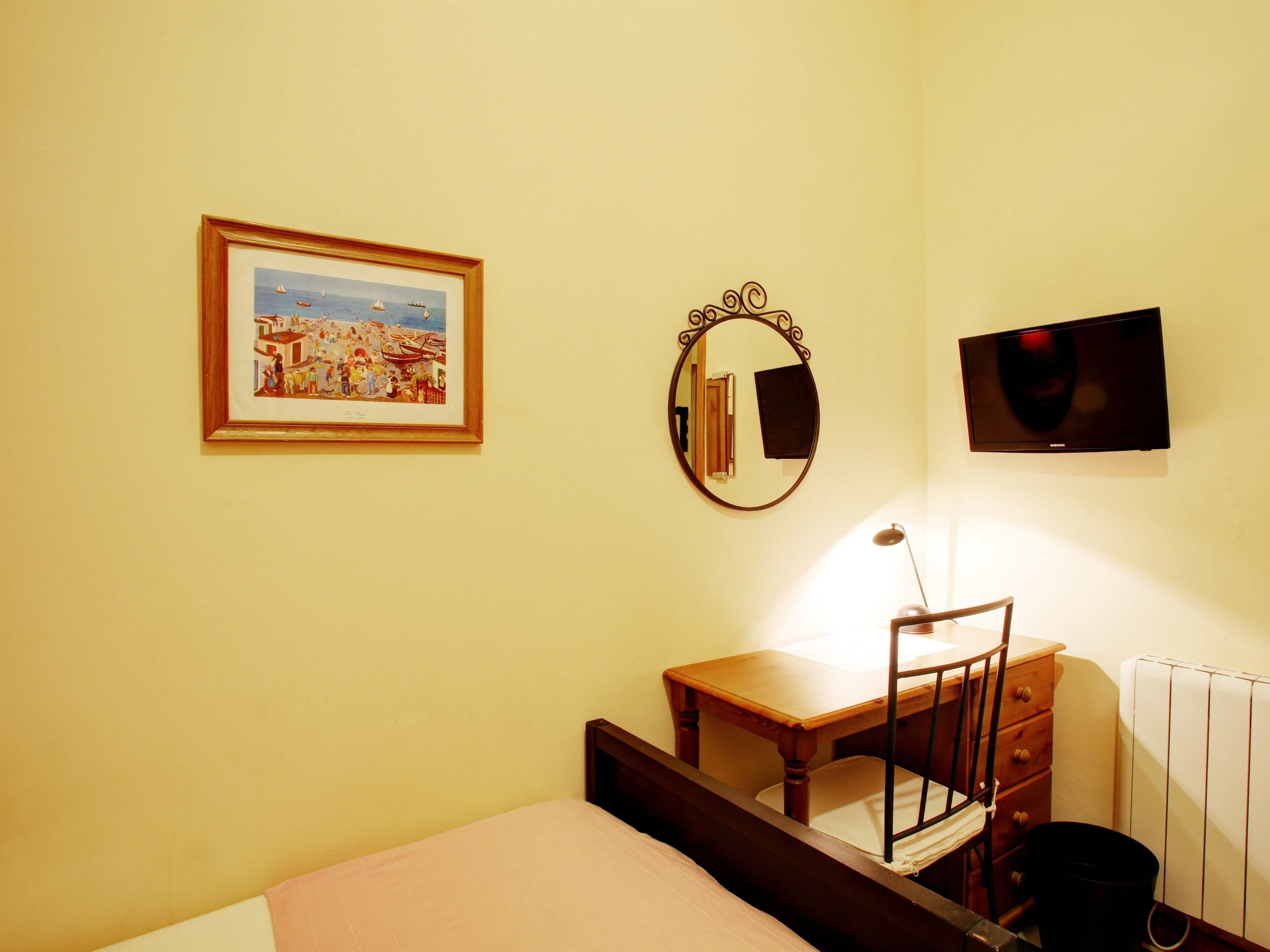 A bedroom with a bed, a desk, a chair, a mirror, a television, and a framed picture on the wall.