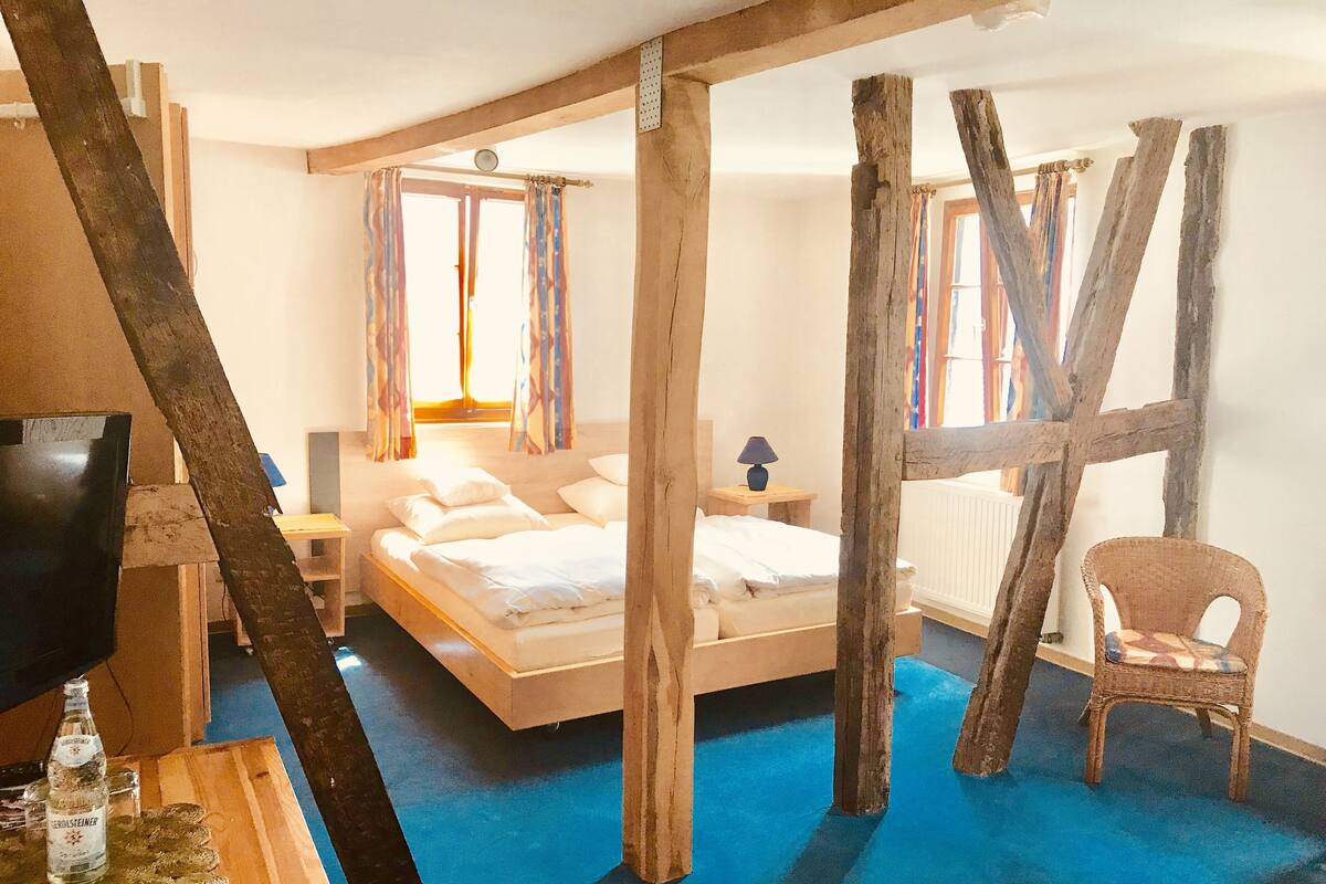 A rustic room with a wooden bed, a chair, and a table with a bottle.