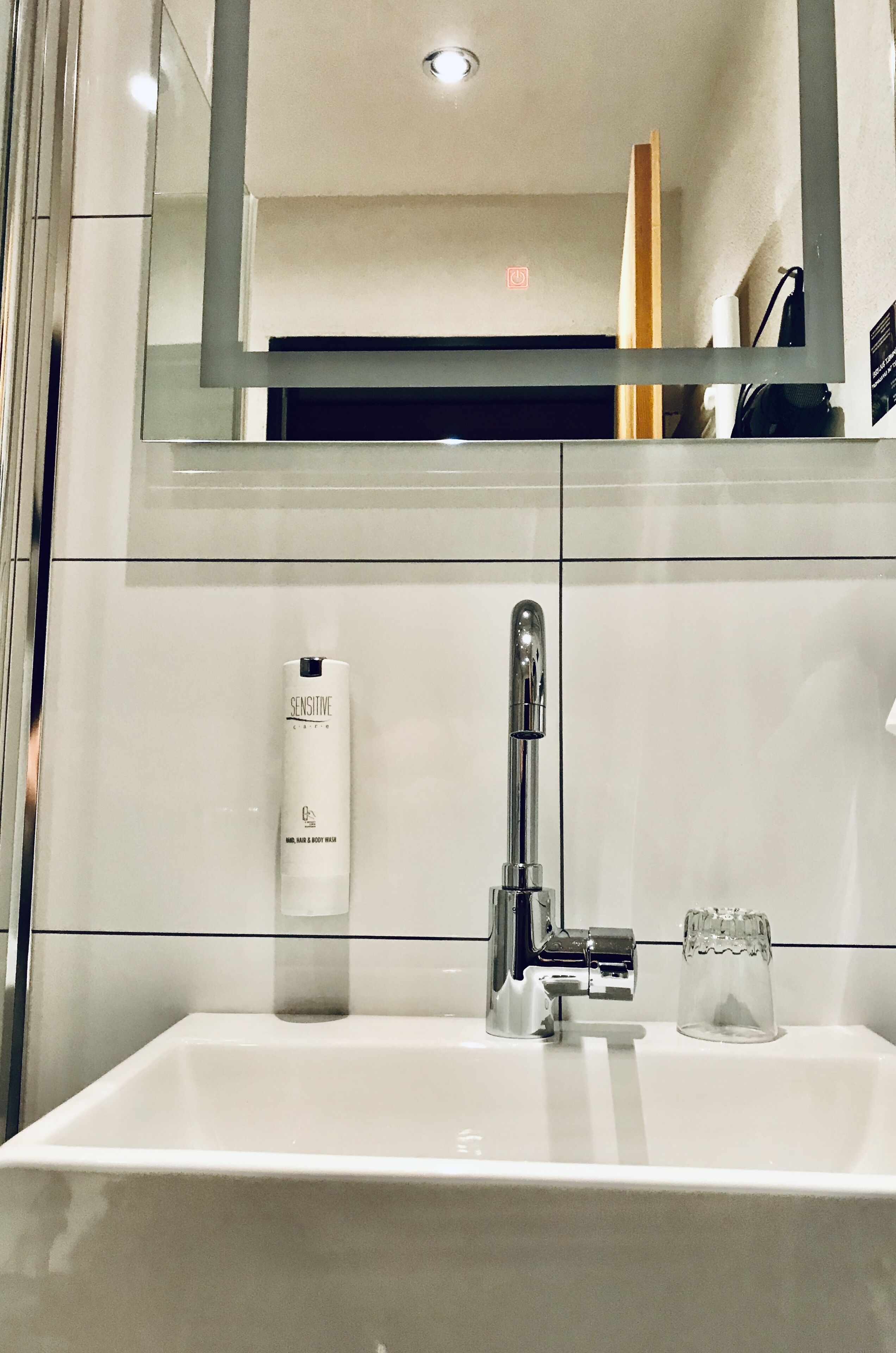 A modern bathroom with a white sink, chrome faucet, and a glass container.