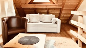 A cozy attic room with a white sofa, a brown leather chair, and a small wooden table. - Hotel Weingut Dehren (Ellenz-Poltersdorf)