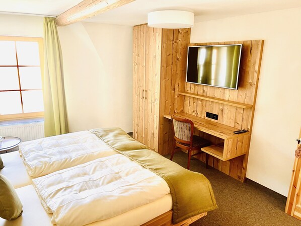 A hotel room with a bed, a desk, a chair, and a TV mounted on a wooden wall. - Hotel Weingut Dehren (Ellenz-Poltersdorf)