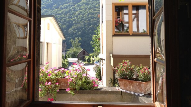 A window view of a building with a mountain backdrop, a stone house, and flower boxes. - Hotel Weingut Dehren (Ellenz-Poltersdorf)