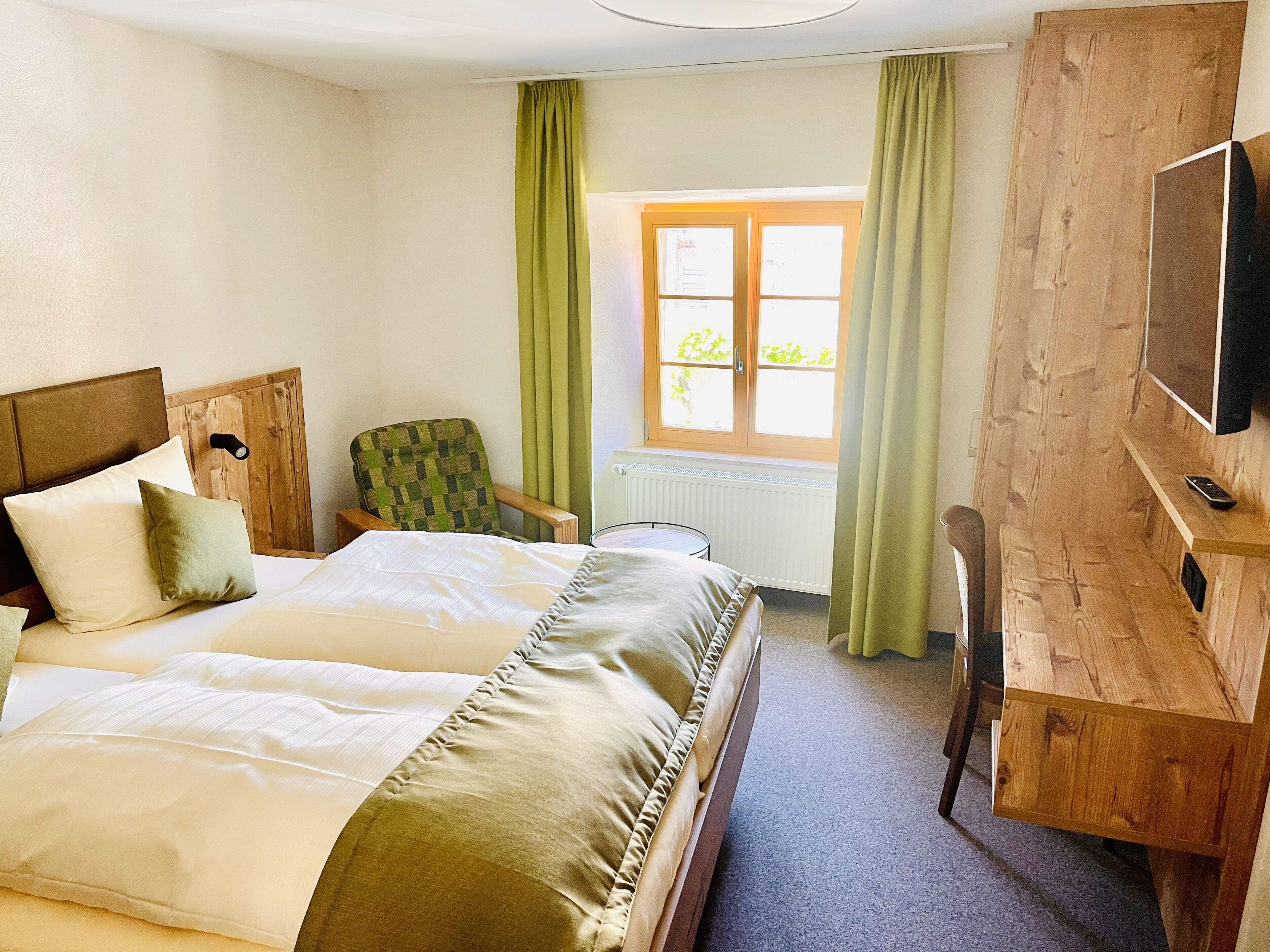 Une chambre à coucher avec un lit, une chaise, une télévision et une fenêtre avec des rideaux.