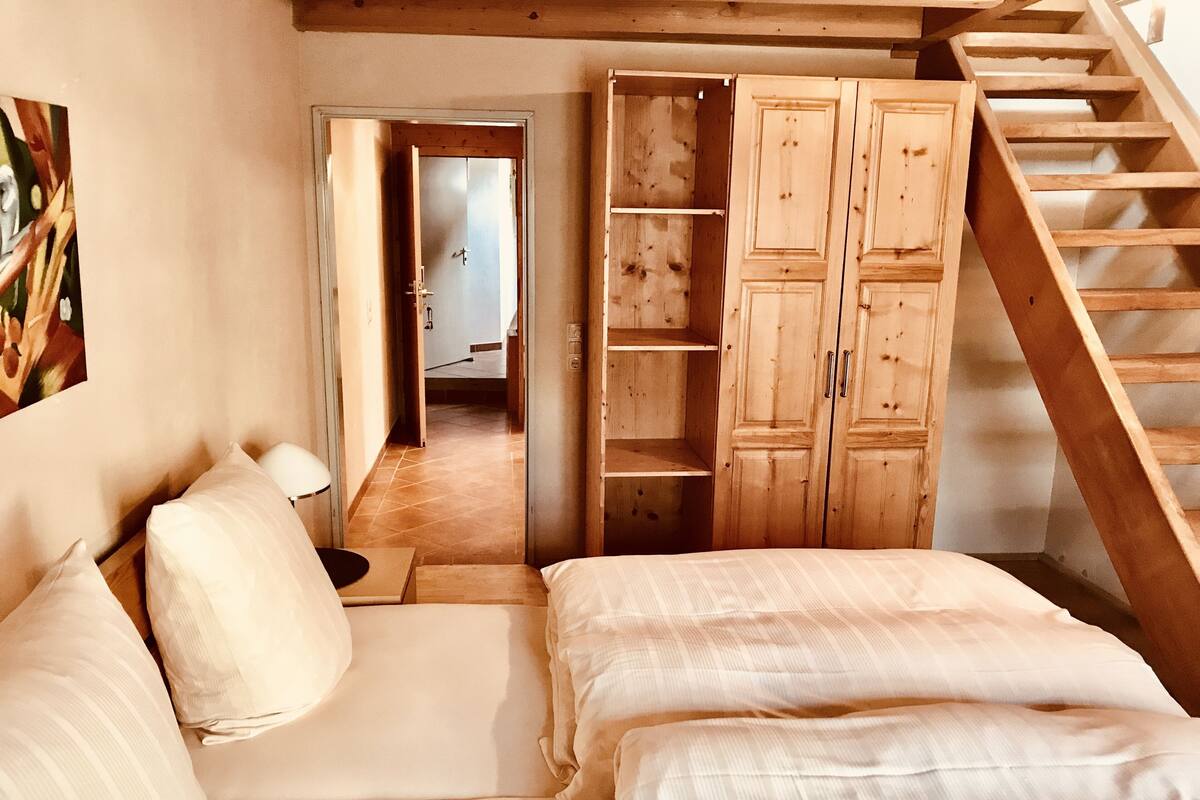 A bedroom with a wooden staircase, a bed with white linens, and a wooden wardrobe.