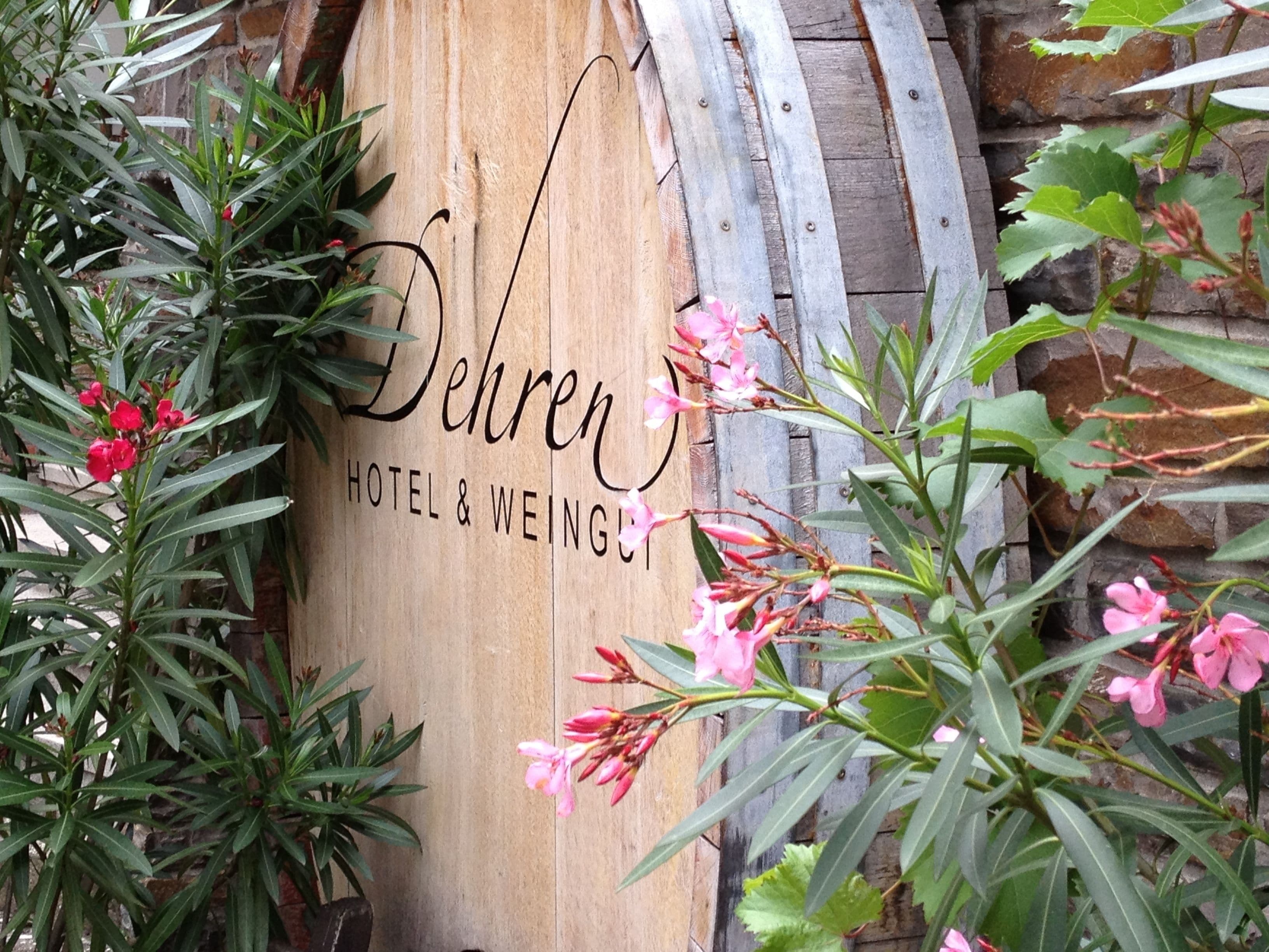 Een houten bord met de naam 'Dehren Hotel & Weingut', omringd door groen en bloemen.