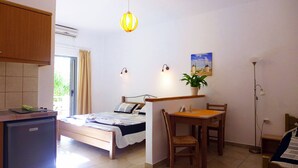 Una habitación pequeña con cama, una mesita, una silla, escritorio, planta en maceta y lámpara de pie.
