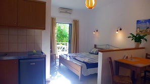 A bedroom with a bed, a desk, a chair, a potted plant, and a view of greenery outside. - Lion-Suites (Apokoronas)