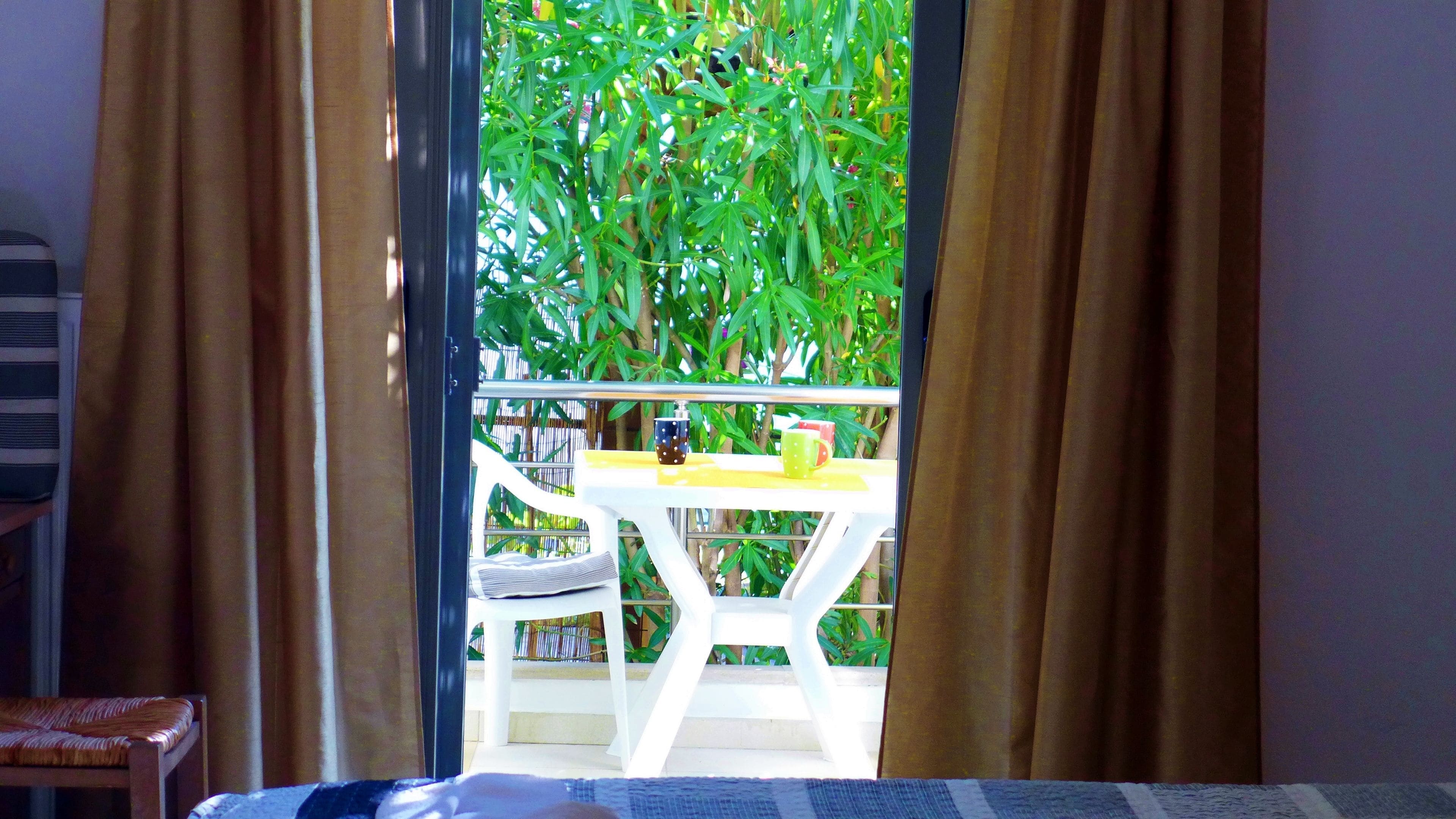 A room with a view of a balcony, a white table with two mugs, and a chair.