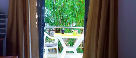 A room with a view of a balcony, a white table with two mugs, and a chair.