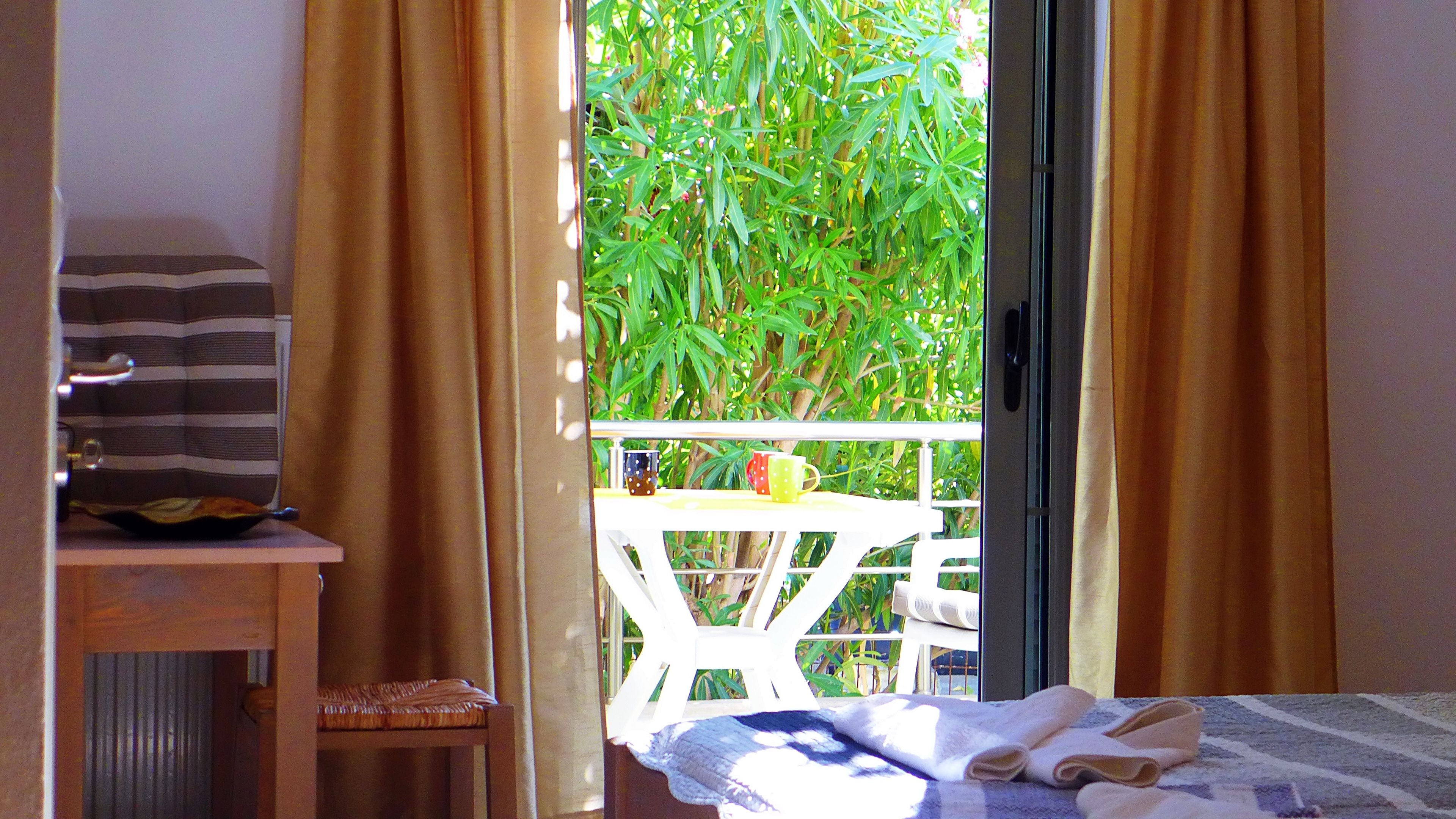 A room with a bed, a small table with colorful mugs, and a view of greenery outside.