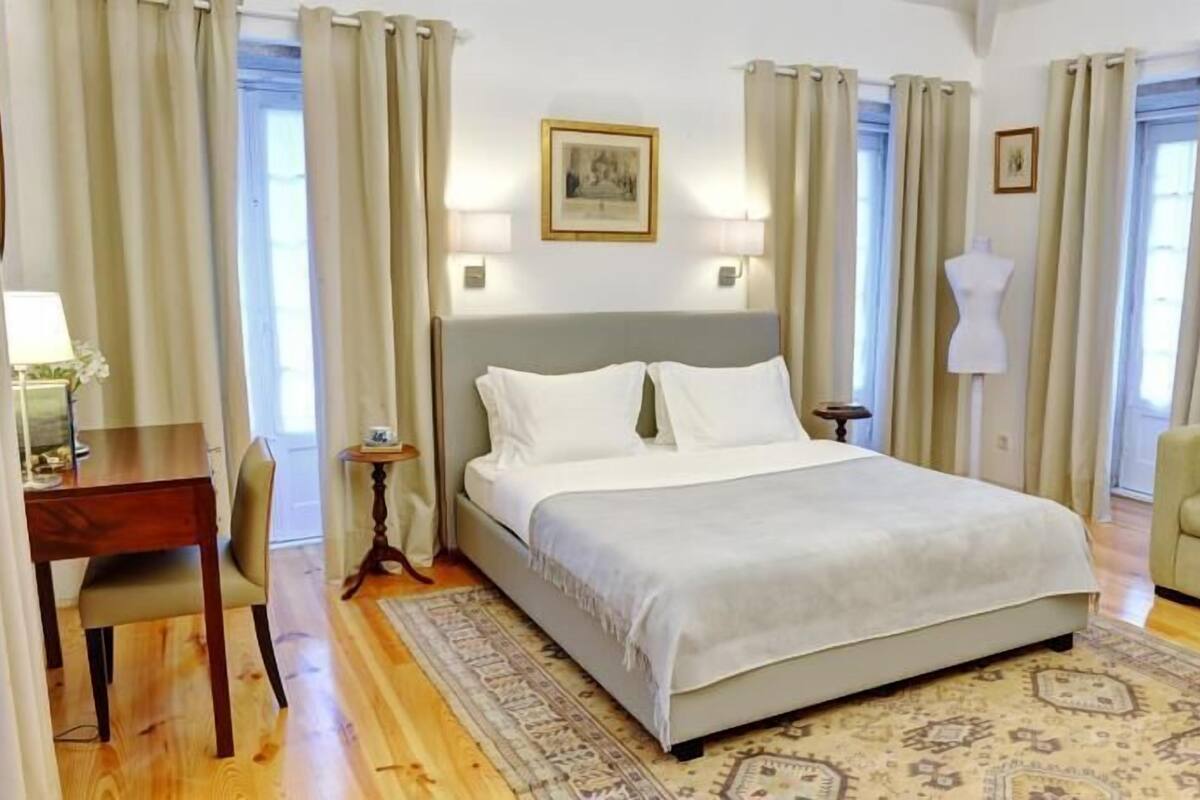 A hotel room with a bed, a desk, a chair, a sofa, and a TV on the wall.