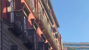 Ein mehrstöckiges Gebäude mit Balkonen, bewölkter Himmel und Blick auf ein weiteres Gebäude in der Ferne.