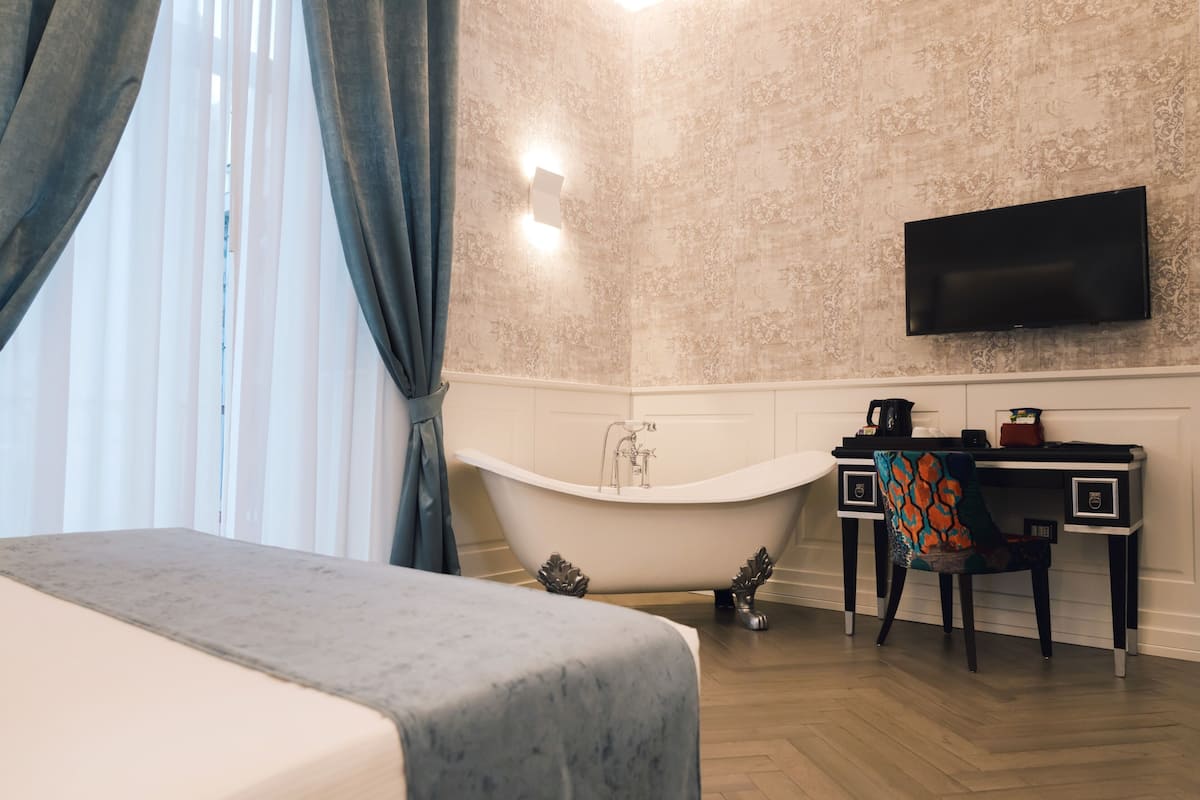Una stanza con un letto, una vasca da bagno, una scrivania con una sedia, una TV a schermo piatto e una parete decorata.