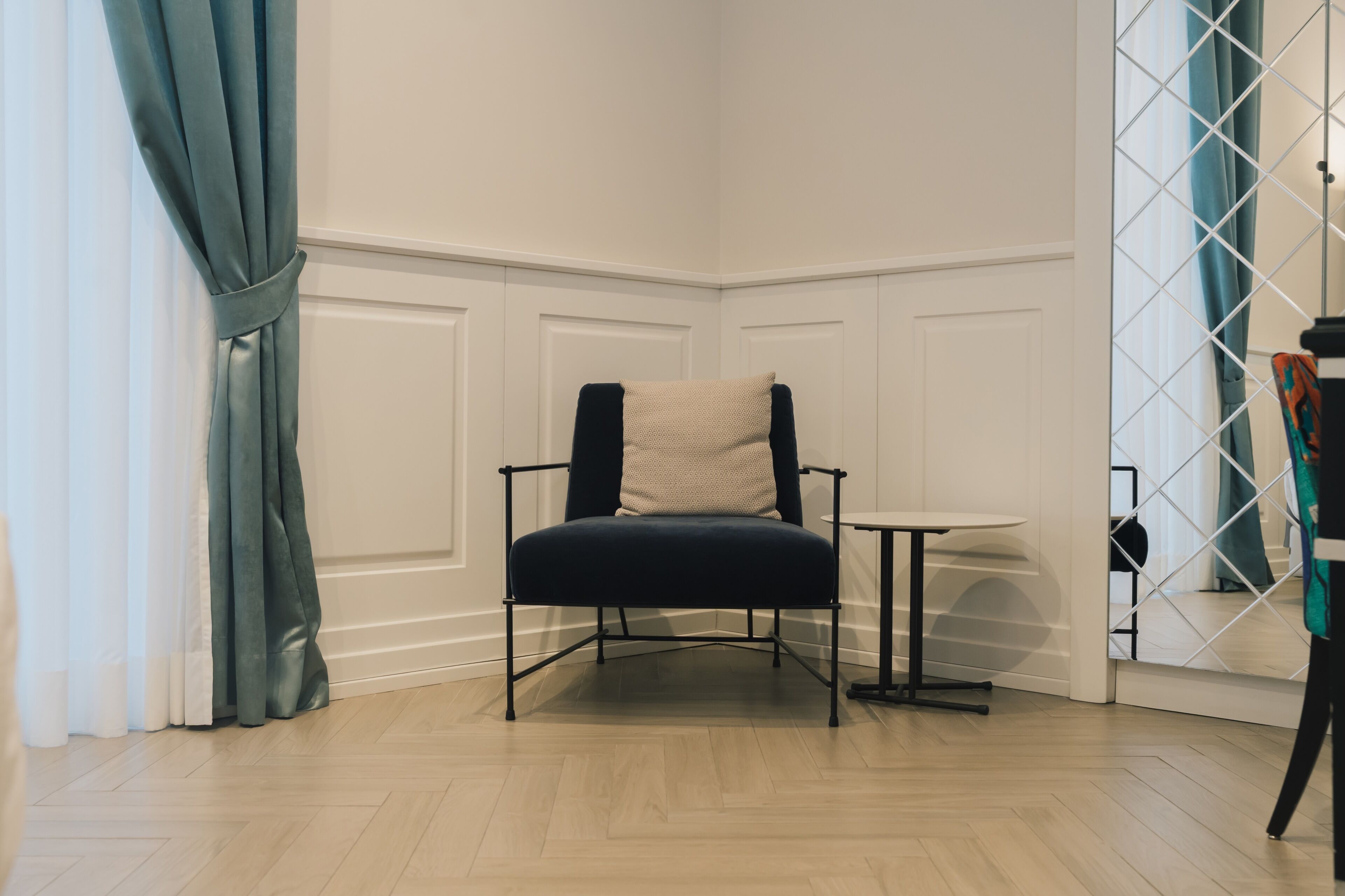 Ein Eckzimmer mit blauem Korpsessel, kleinem runden Tisch und einer weißen Wand mit Wandverkleidung.