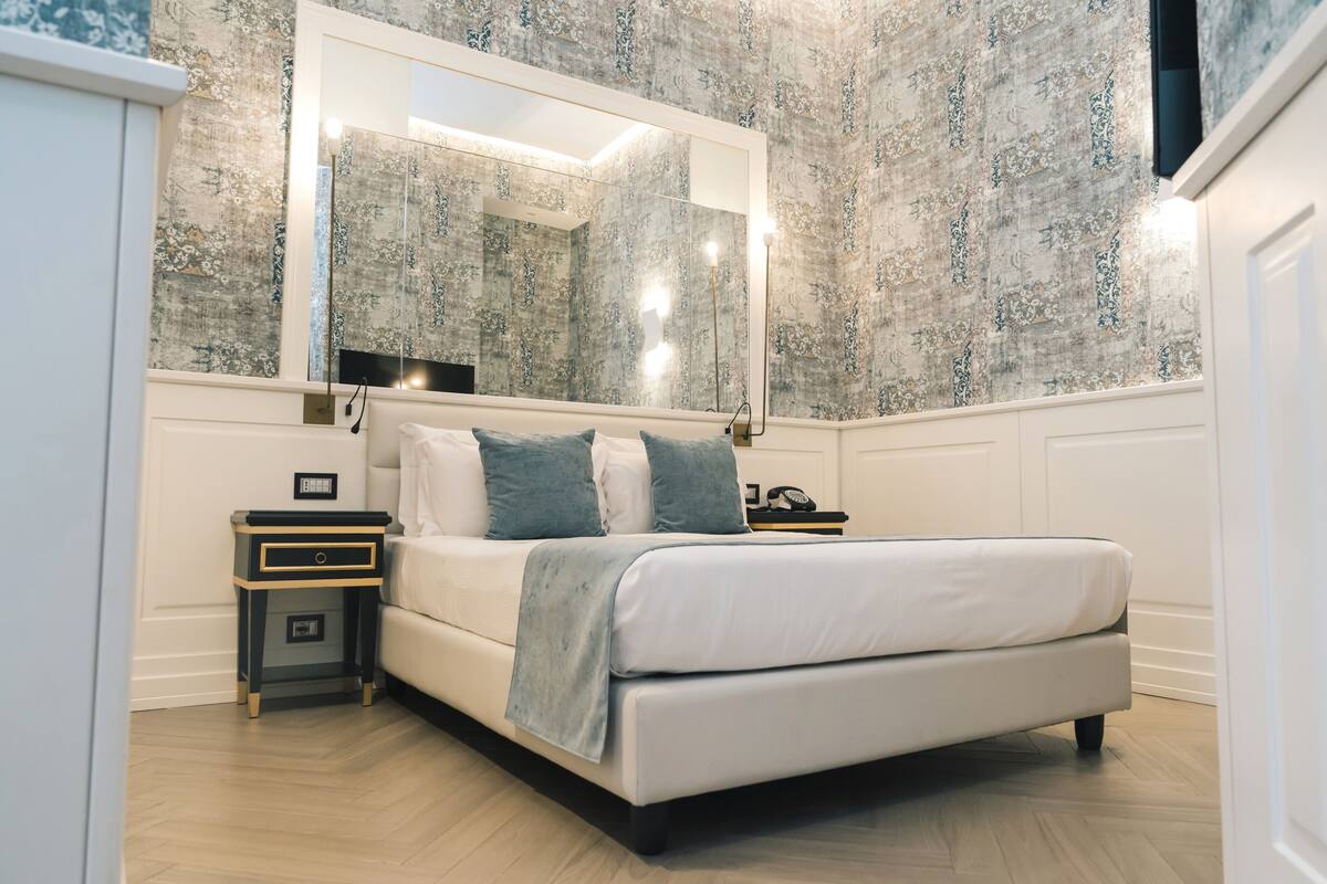 Una camera da letto con un letto grande, un comodino, uno specchio e carta da parati decorata.