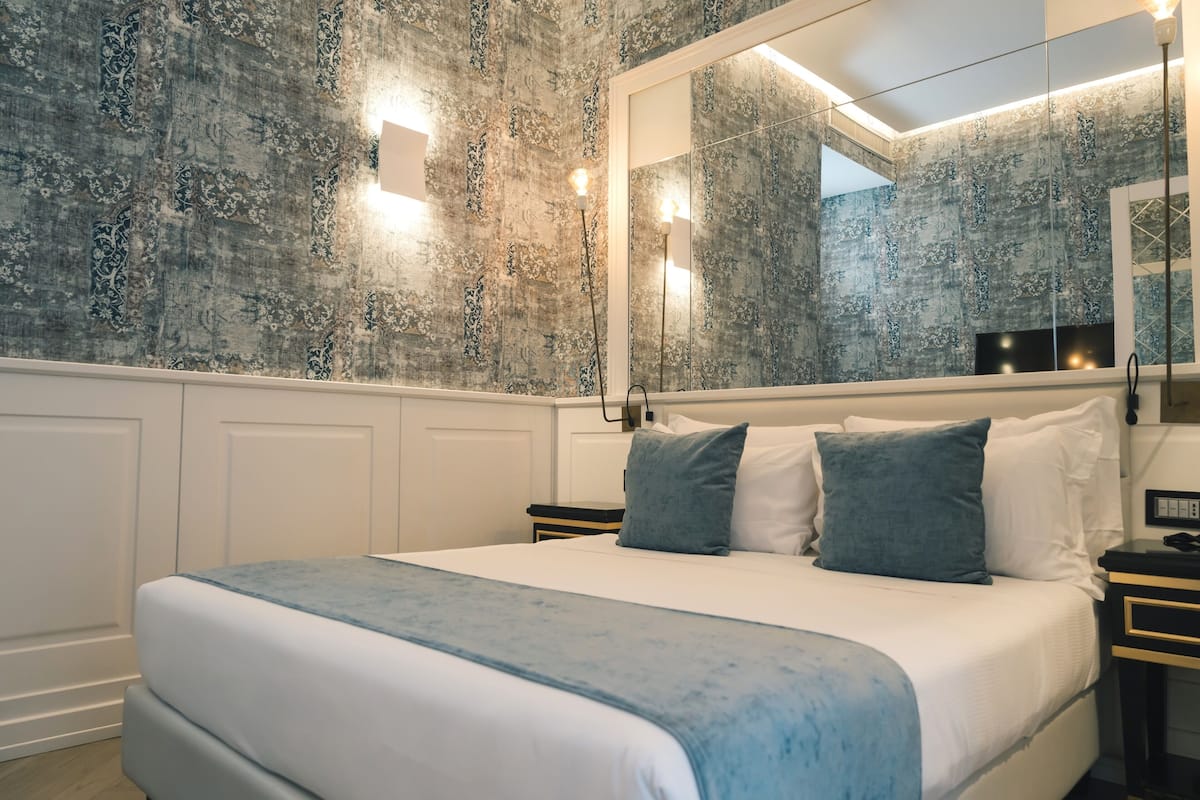Camera da letto con un letto grande, un comodino, uno specchio e una parete con motivo decorativo.