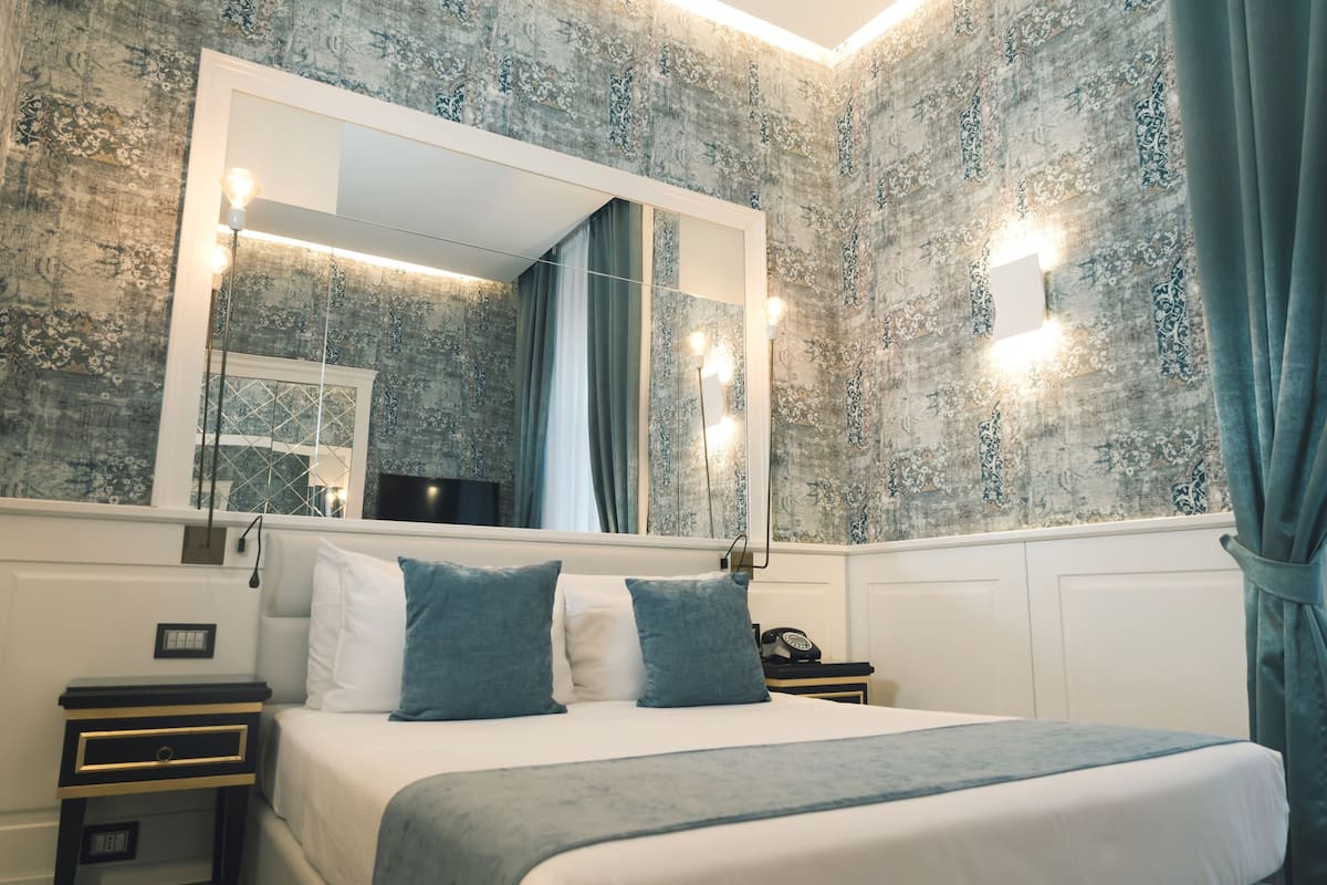 Una camera da letto con un letto grande, uno specchio, un comodino e una lampada a parete.