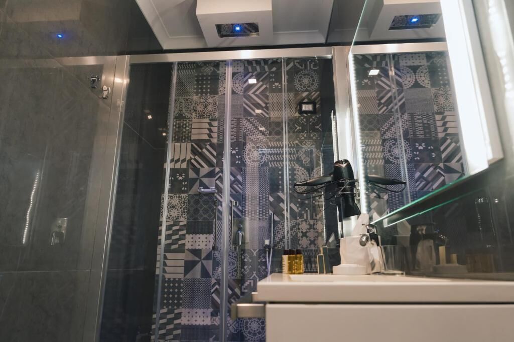 A modern bathroom with patterned tiles, a glass shower enclosure, and a white countertop with a black lamp.