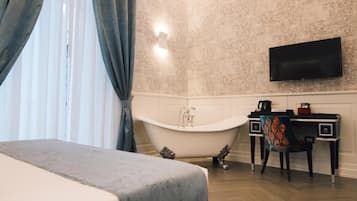 Quarto com cama, banheira, escrivaninha com cadeira e televisão de tela plana na parede.