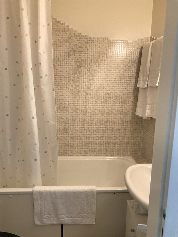 Un baño con bañera, un lavamanos blanco y una cortina de ducha con estampado floral.