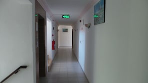 A hallway with a fire extinguisher, exit signs, and a framed picture on the wall.