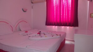 Et pink-farvet hotelværelse med seng, puder, et sengebord og et vindue med pink gardiner.