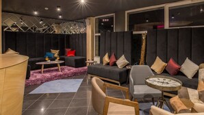 Un espacio lounge moderno con un conjunto de sofás, una mesa redonda de centro y un reloj sobre una mesita auxiliar.