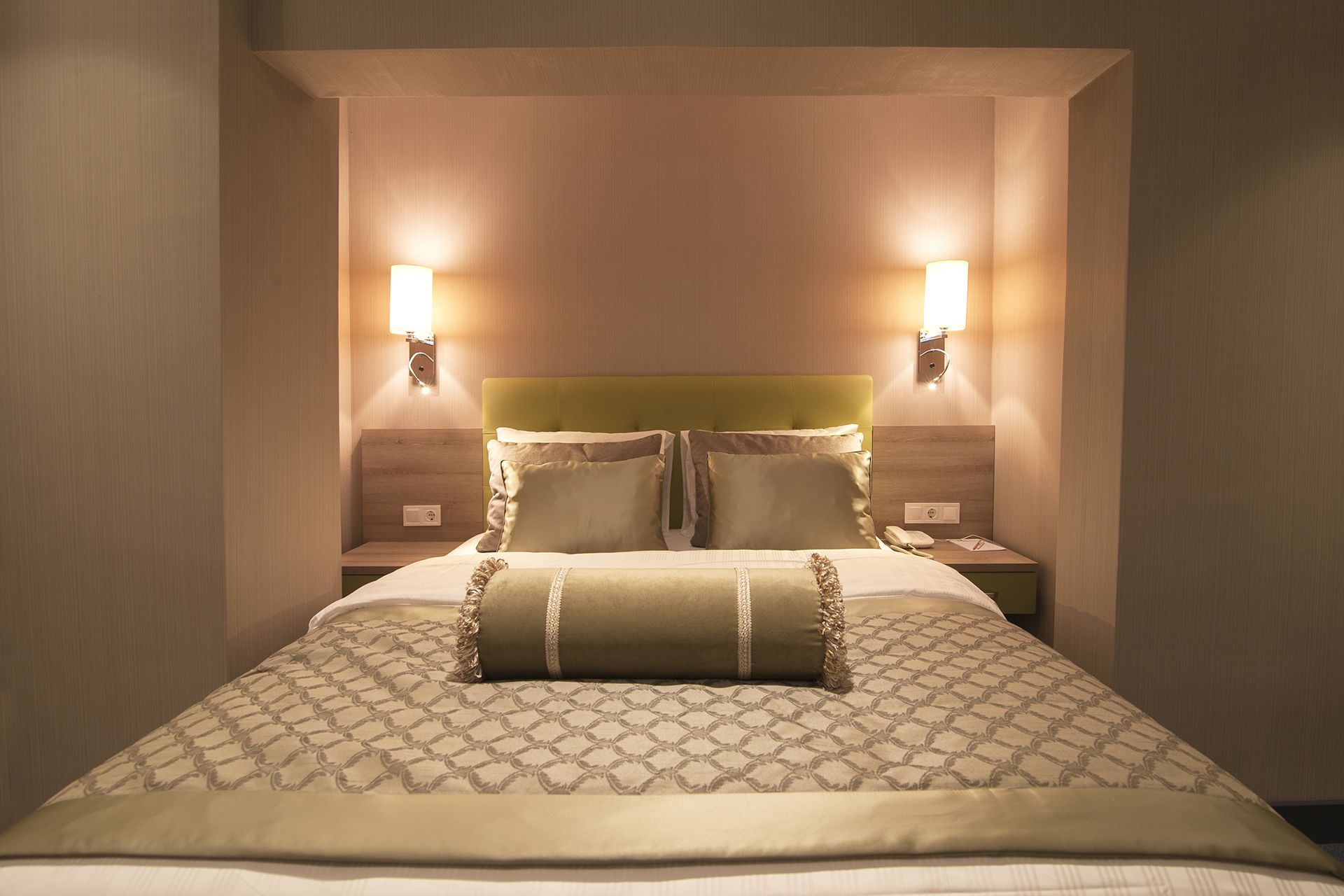 A neatly made bed with a patterned bedspread and two pillows, flanked by two bedside tables with wall-mounted lamps.