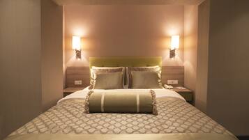A neatly made bed with a patterned bedspread and two pillows, flanked by two bedside tables with wall-mounted lamps.