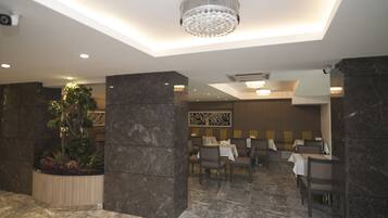 Un restaurante moderno con suelos de mármol, pilares de piedra oscura y una araña.