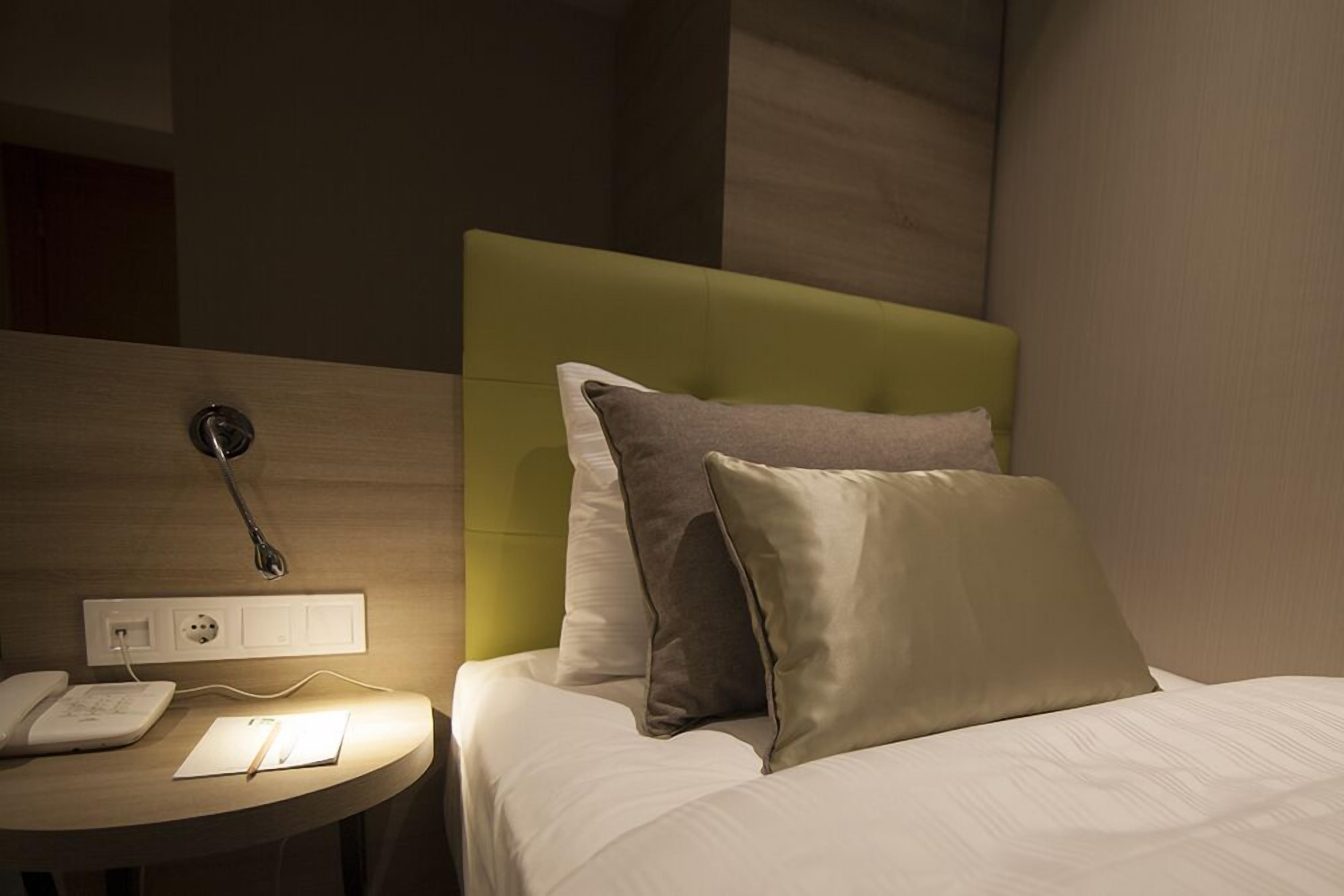 Ett hotellrum med en säng, ett sängbord med en lampa och ett vägguttag.