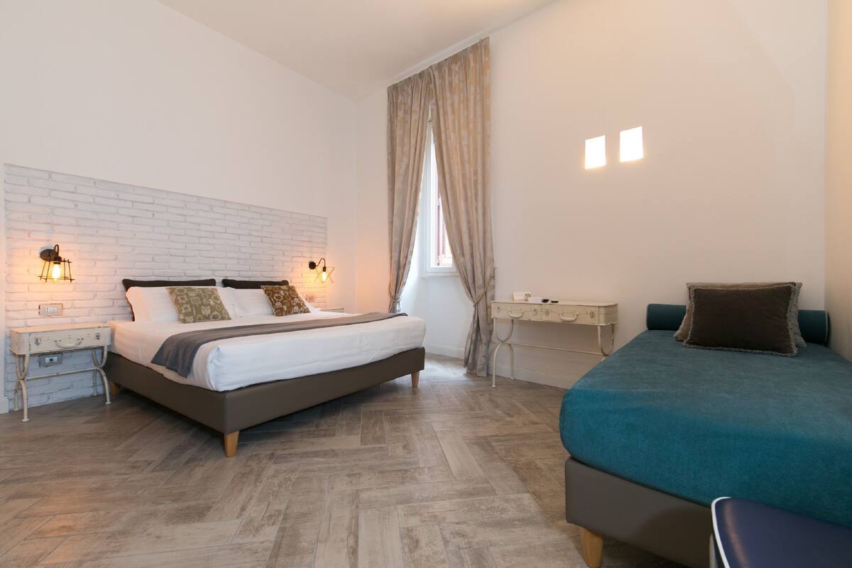 A bedroom with a bed, a desk, and a window with curtains.