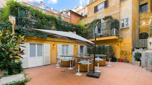 An outdoor patio area with round tables and chairs, surrounded by yellow walls and greenery. - Trevi Contemporary Suite (Rome)