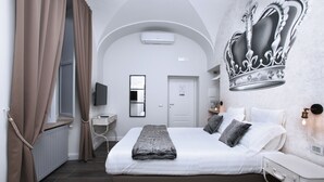 A bedroom with a large bed, a flat-screen TV, a desk, and a wall-mounted air conditioner. - Trevi Contemporary Suite (Rome)