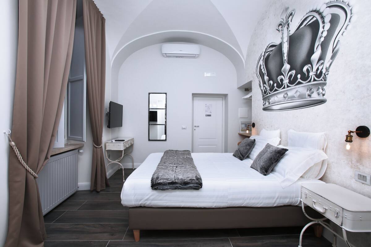 A bedroom with a large bed, a flat-screen TV, a desk, and a wall-mounted air conditioner.