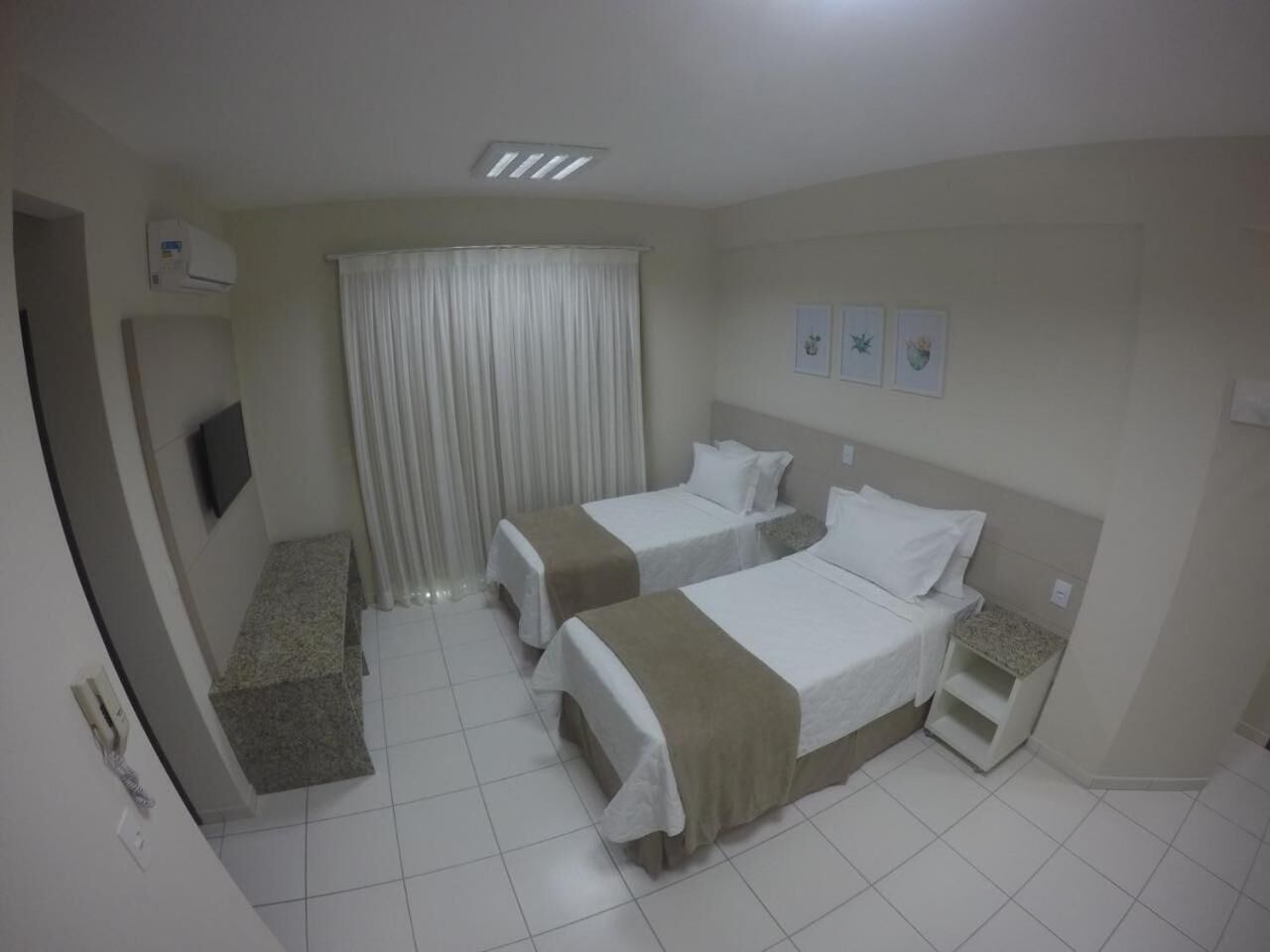 Habitación de hotel con dos camas, televisión, ventana con cortinas y un escritorio pequeño.