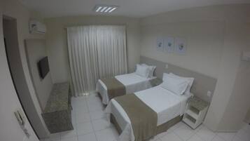Habitación de hotel con dos camas, televisión, ventana con cortinas y un escritorio pequeño.