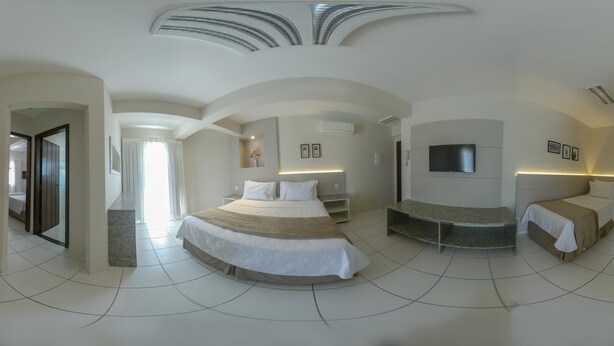 A modern hotel room with a curved ceiling, a large bed, a TV, and a separate seating area. - Pousada Doluar (Penha)