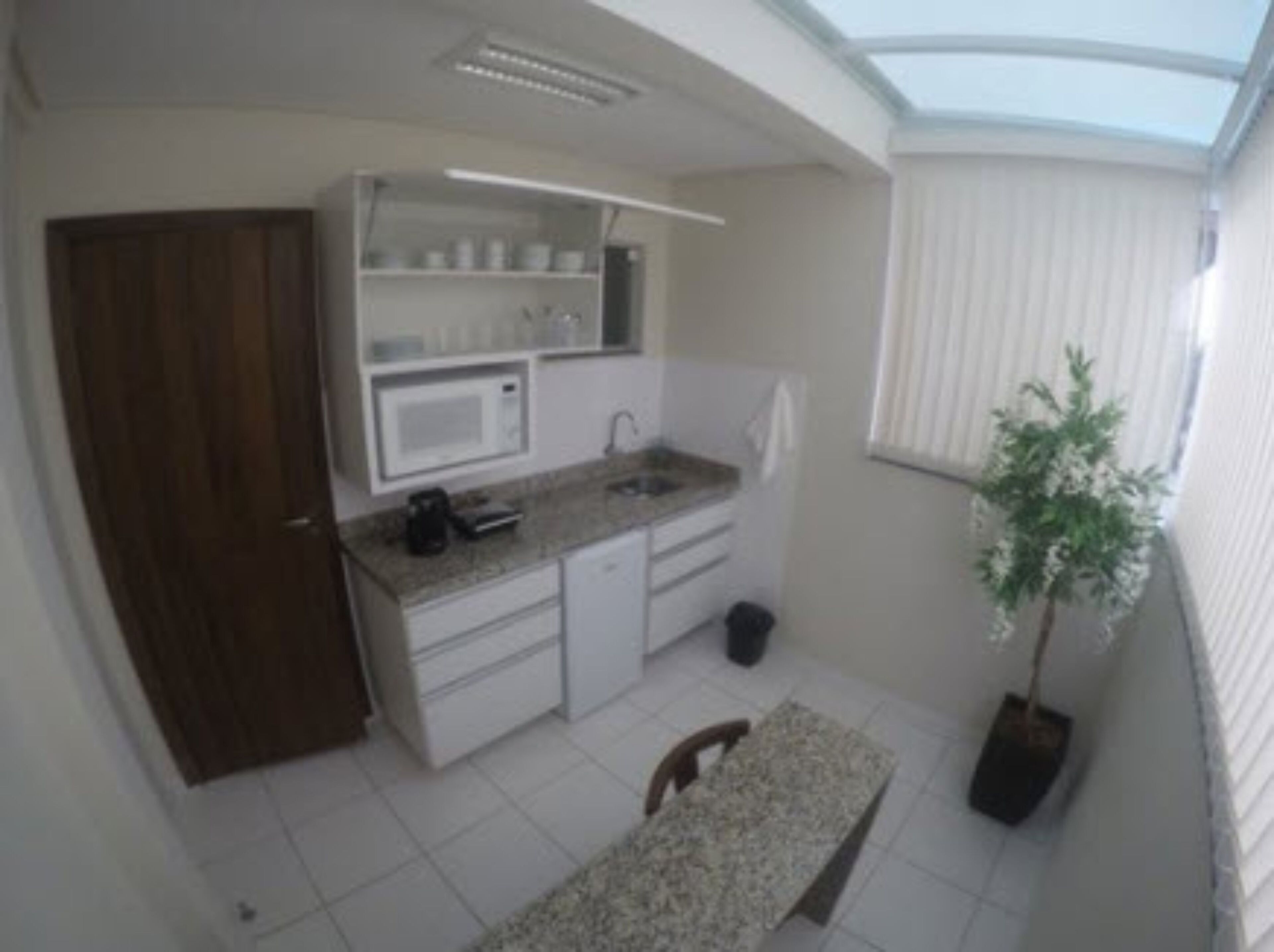 Cocina compacta con armarios blancos, microondas y fregadero. Hay un pequeño cubo de basura y una planta en maceta.