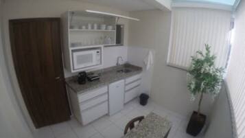 Cocina compacta con armarios blancos, microondas y fregadero. Hay un pequeño cubo de basura y una planta en maceta.