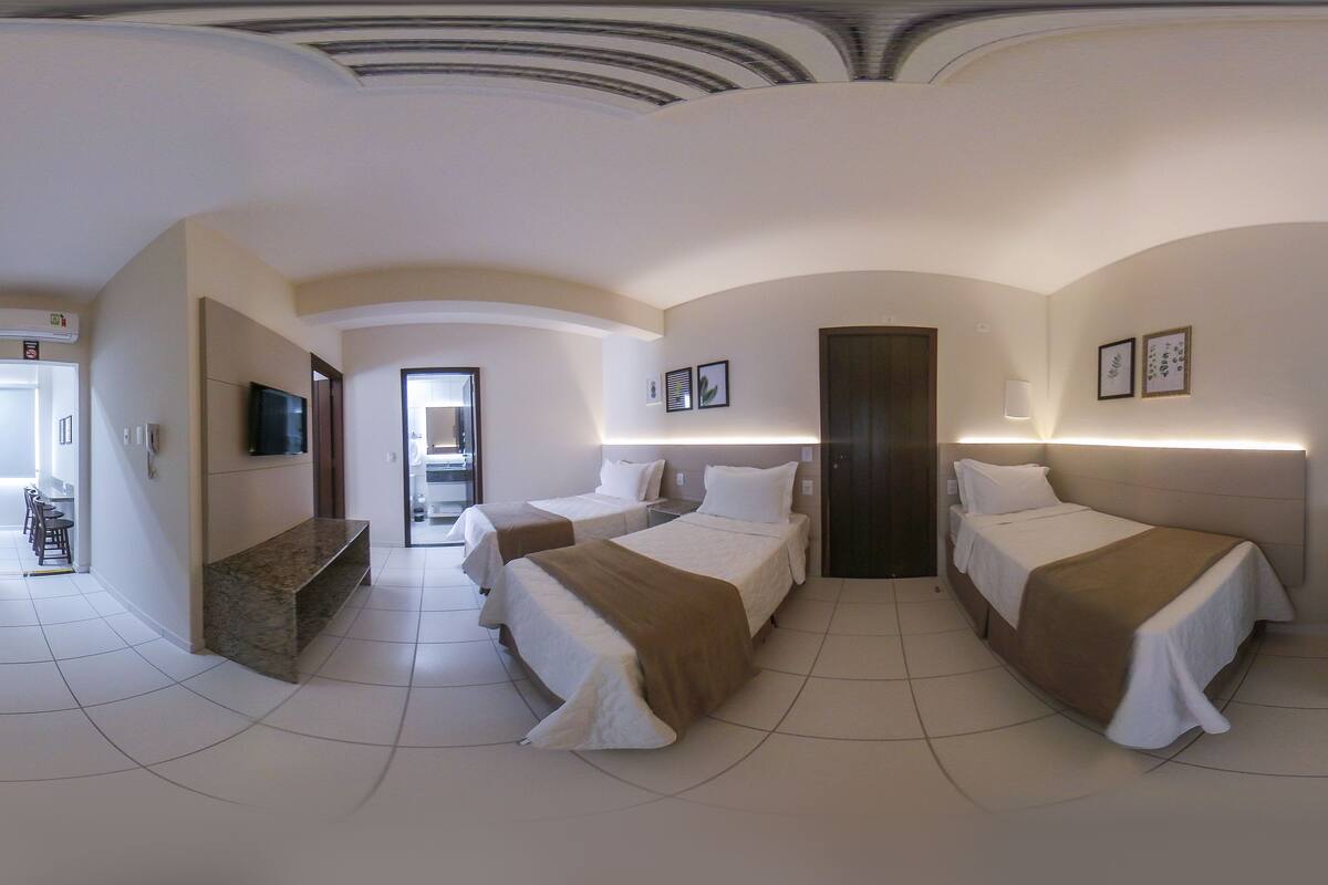 A hotel room with two beds, a TV, a desk, and a bathroom visible through an open door.