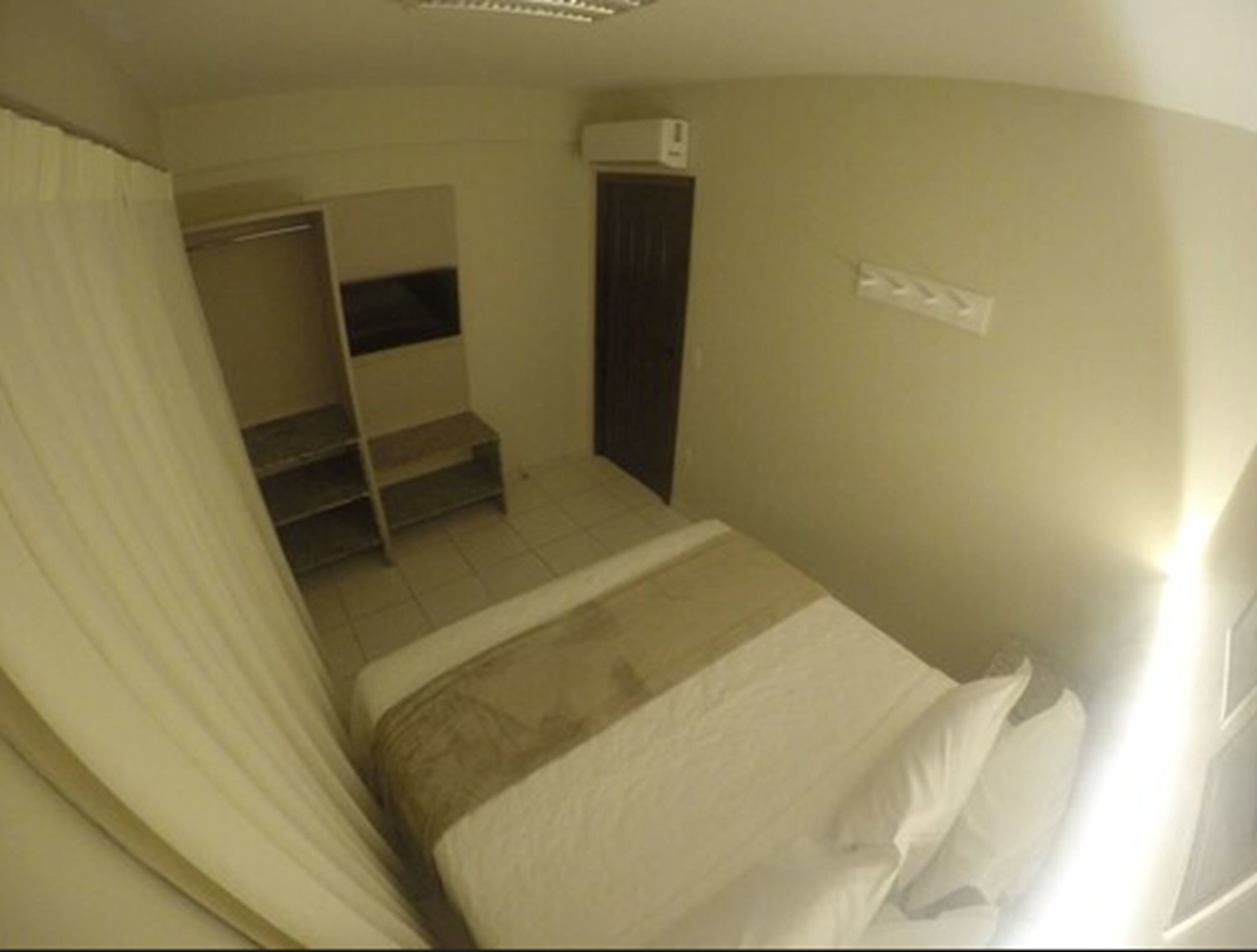 Una stanza piccola e poco illuminata con un letto singolo, una TV integrata e un armadio.