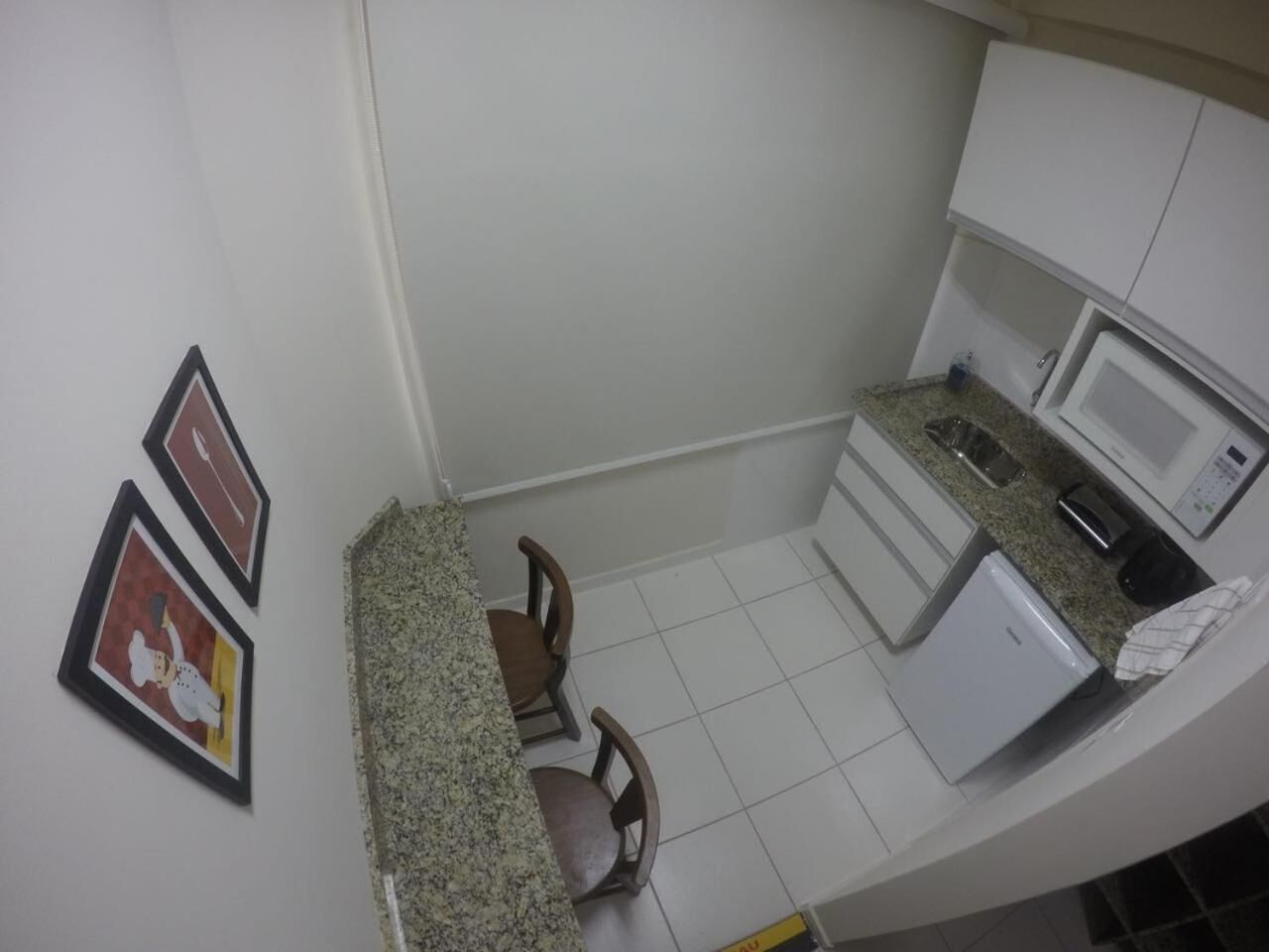 Uma cozinha compacta com micro-ondas, um refrigerador pequeno e um espaço de refeições com duas cadeiras.
