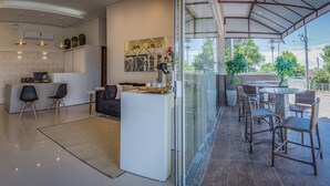 A modern hotel lobby with a reception desk, seating area, and a glass partition leading to an outdoor patio with wicker furniture. - Pousada Doluar (Penha)