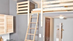 A compact kitchen with wooden cabinets, a sink, and a ladder leading to a loft bed. - Smart Rooms for Rent (Kraków)