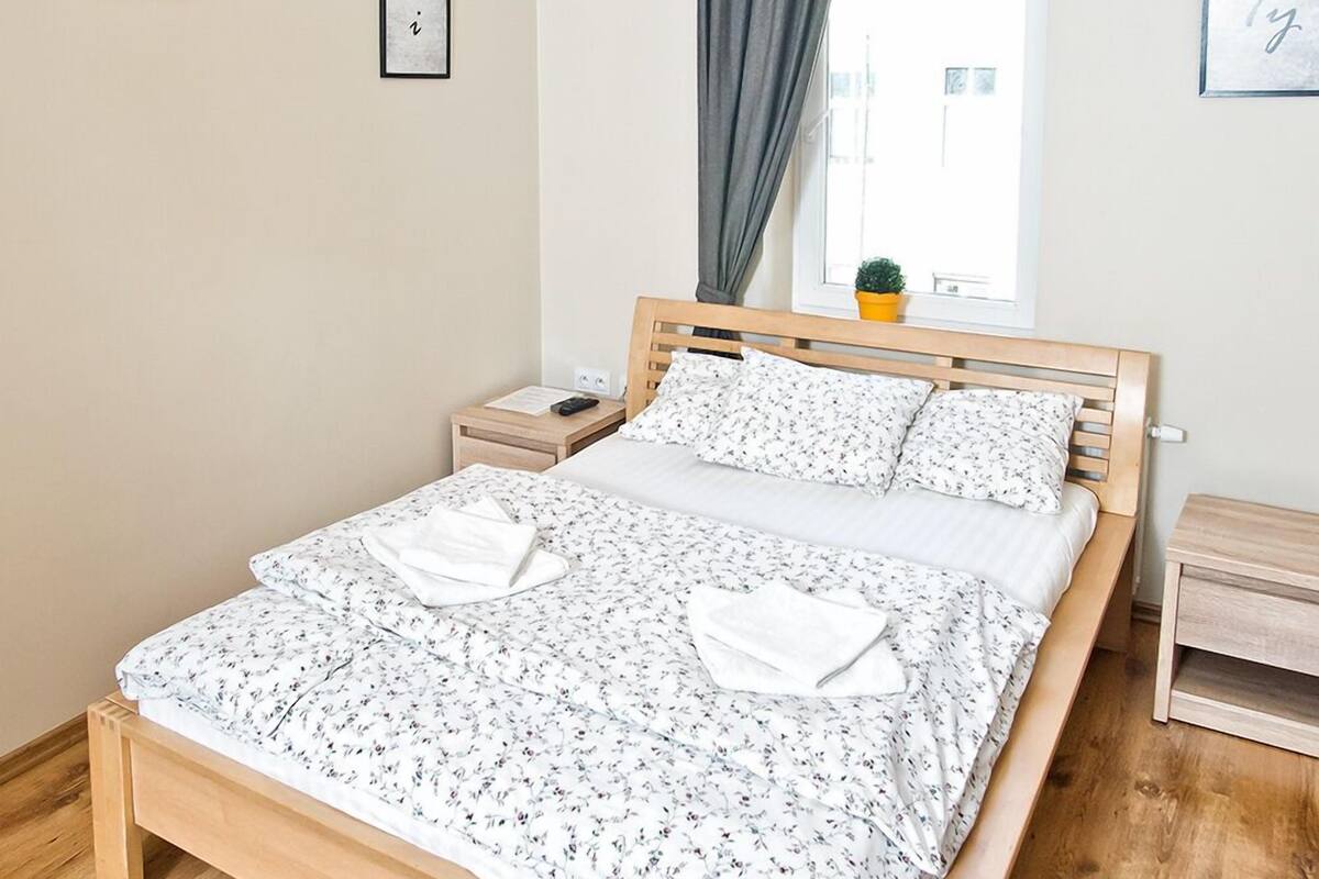 Una cama bien tendida con ropa de cama floral, cabecero de madera, mesitas de noche y una ventana con cortinas.